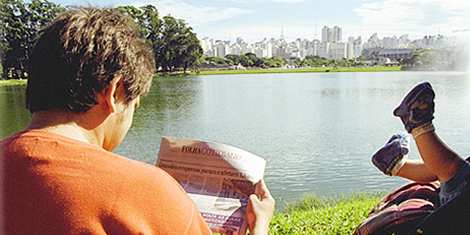 Un joven lee la Folha al lado de su hijo, en el csped del parque Ibirapuera en So Paulo