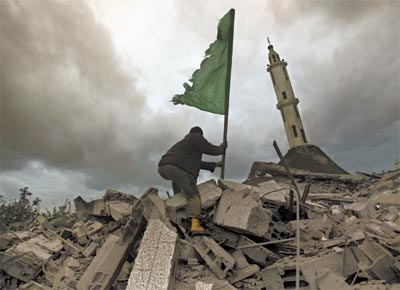 Homem finca bandeira do grupo Hamas ao lado de mesquita destruda na cidade de Gaza pelos bombardeios areos israelenses