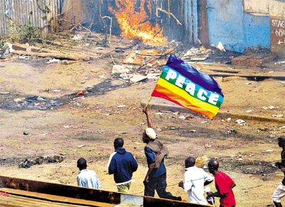 Jovem carrega bandeira com a palavra 'paz' ao lado de casa incendiada num subrbio de Nairbi