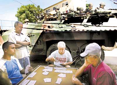 Moradores de favela no Rio jogam cartas enquanto soldados do Exrcito patrulham a rea num blindado