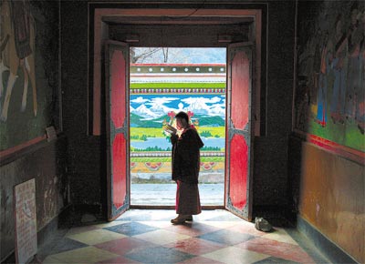 Monge tibetano reza na entrada de mosteiro em Sichuan