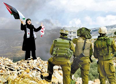 Observada por soldados israelenses, palestina faz protesto em Bilin, na Cisjordnia, contra ofensiva de Israel na faixa de Gaza