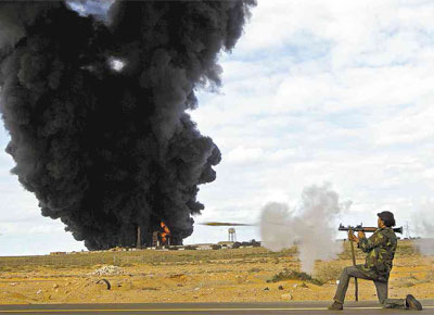 Rebelde anti-Gaddafi dispara granada diante de terminal de armazenamento de gs atingido por bombardeio