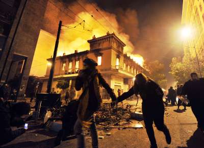 Manifestantes correm no centro de Atenas e passam diante de prdio em chamas, durante os confrontos com a polcia