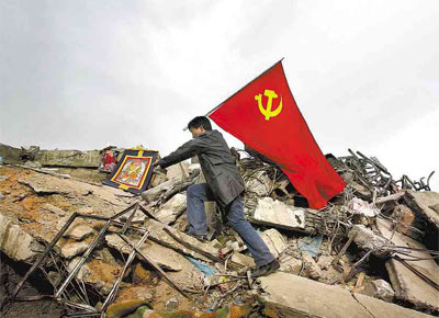Com a bandeira do Partido Comunista da China, homem anda sobre escombros do terremoto que matou, segundo o governo, 1.144