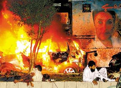 Feridos no ataque ao comboio de Benazir Bhutto em Karachi esperam por socorro perto de um dos veculos incendiados na ao