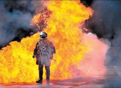 <b>T QUENTE:</b> Policial em meio a chamas de coquetis molotov lanados por manifestantes em Atenas durante protesto contra medidas de austeridade do governo grego