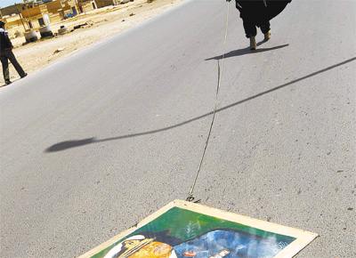 Rebelde arrasta quadro do ditador da Lbia,<br> Muammar Gaddafi, em estrada de Bin Jawad