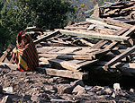 Mulher senta perto de escombros de casa destruda