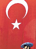 Mulheres passam diante da bandeira da Turquia, pas que sofreu fuga de capitais