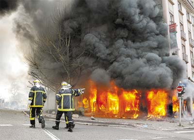 Bombeiros andam em frente ao hotel cujo piso trreo foi consumido pelo fogo, colocado por manifestantes em ato contra a Otan