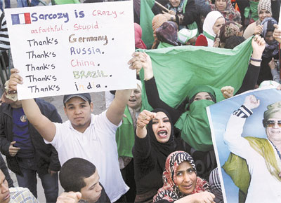 OBRIGADO, BRASIL: Manifestantes pr-Gaddafi em Trpoli mostram pster do ditador e cartaz que chama Sarkozy